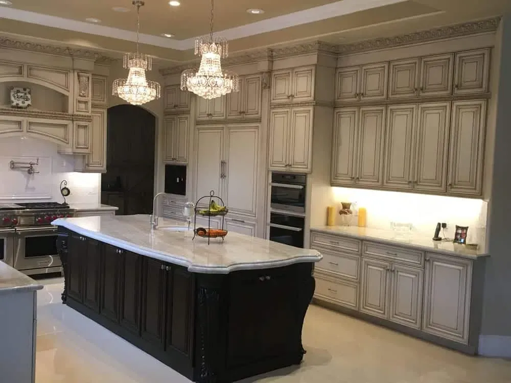 Ornate glazed kitchen with two crystal chandeliers, a dark island and raised-panel cabinetry