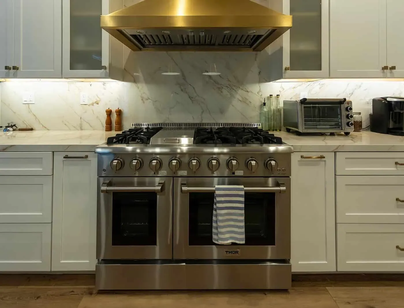 Stainless double-oven range beneath a brass hood with a marble slab backsplash