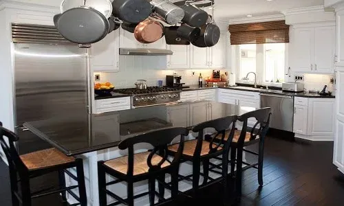 Stainless professional range with a hanging pot rack and a dark island with bar stools