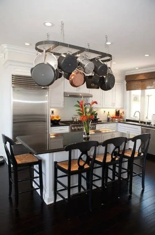 Stainless range with a pot rack above a dark island with bar stools