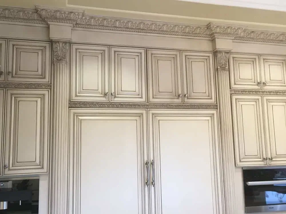 Tall glazed cream cabinetry with panelled appliance fronts and heavy crown moulding