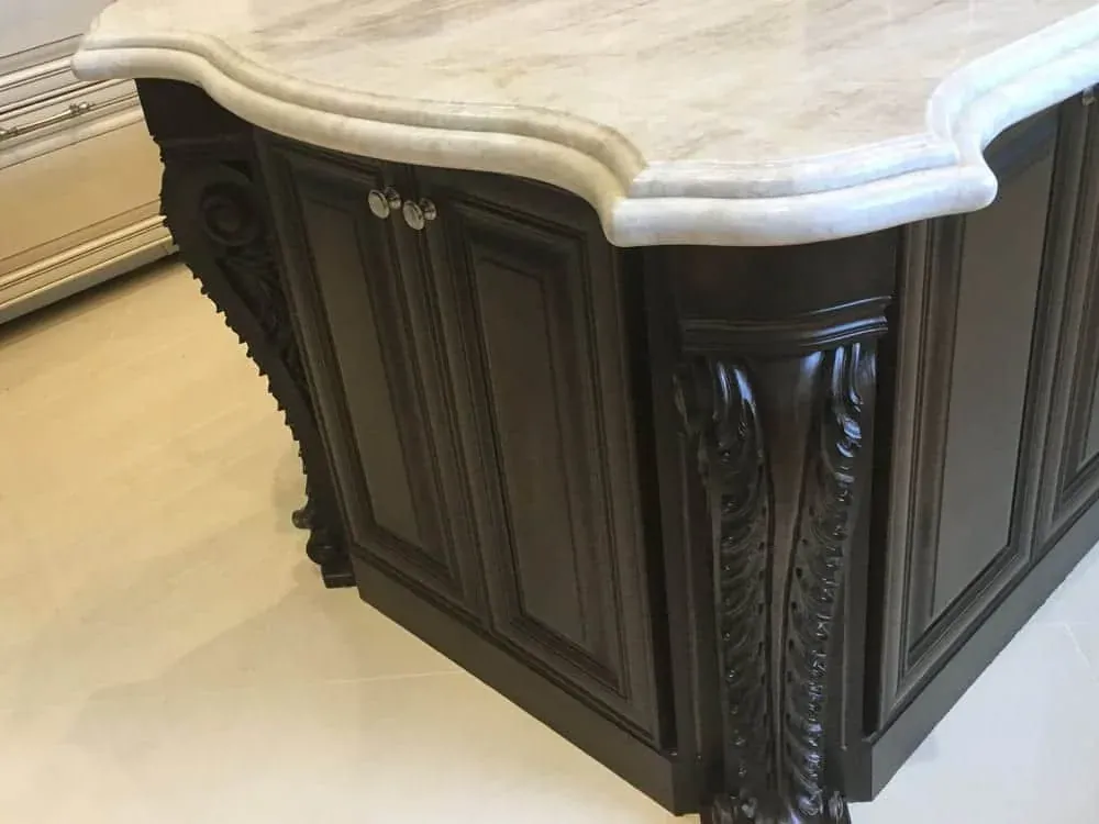 Thick travertine island top with an ogee edge over a dark carved island base