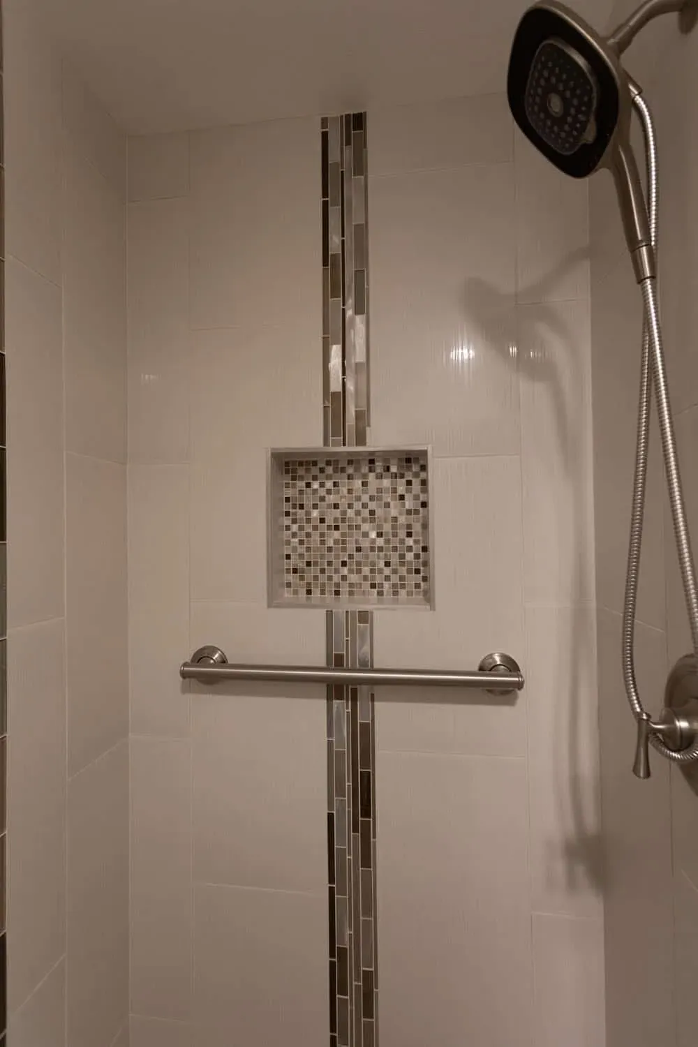 Tiled shower with a mosaic niche, grab rail and handheld shower