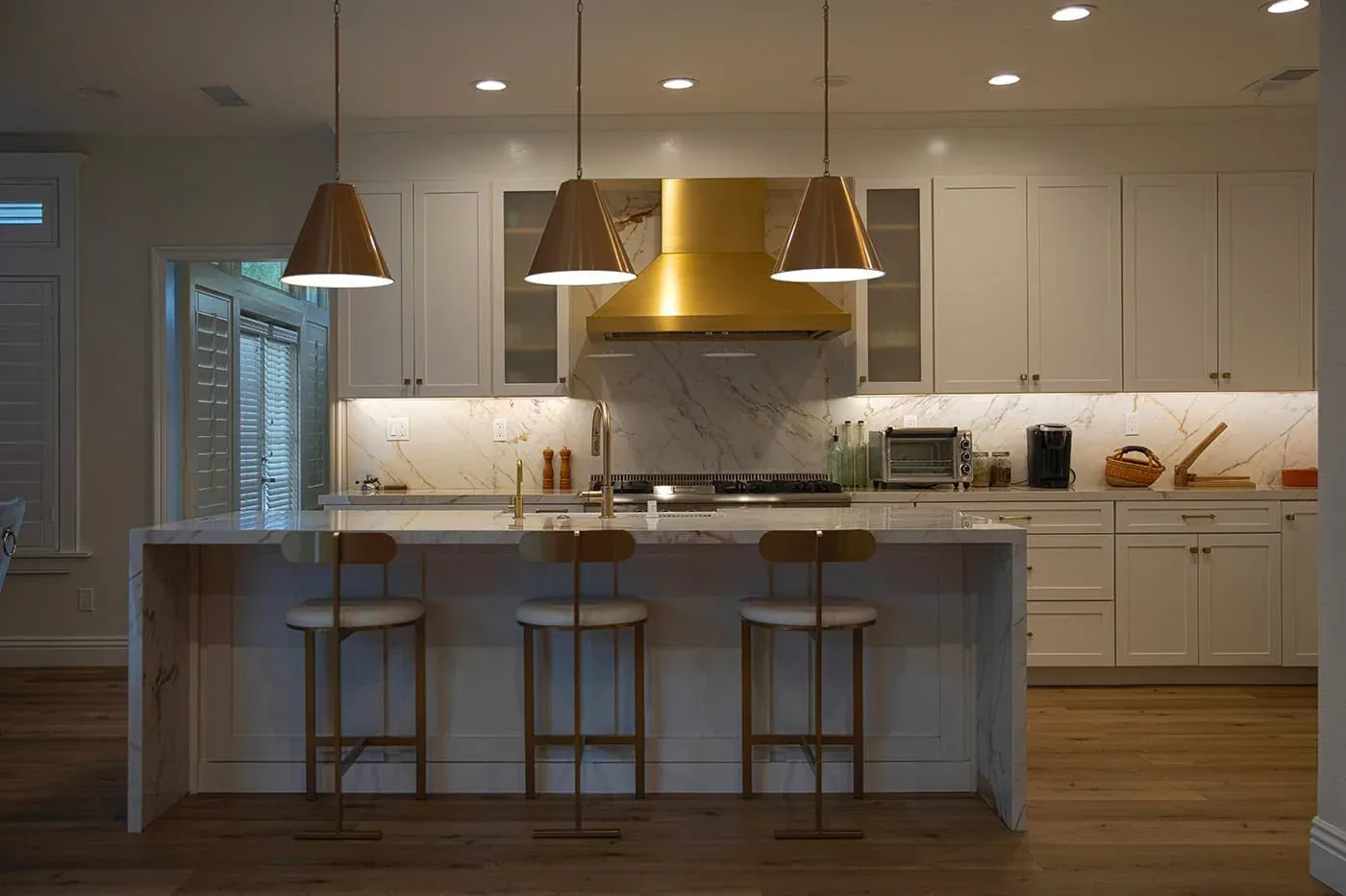 View across the marble island toward the brass hood and range wall