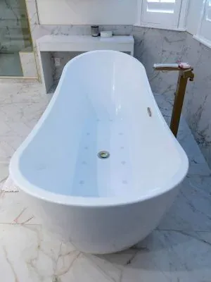 White freestanding soaking tub with a floor-mounted filler against a marble wall