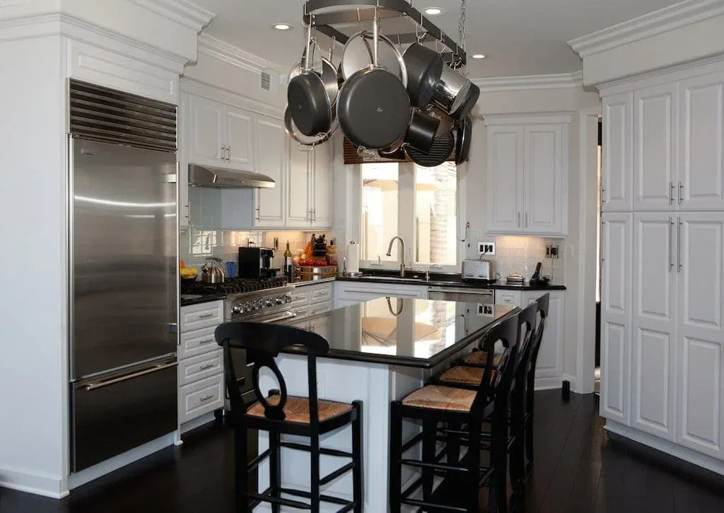 White kitchen with a pot rack, dark island and bar stools