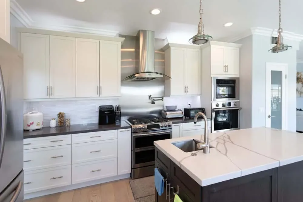 White kitchen with a stainless hood, quartz island and wall ovens
