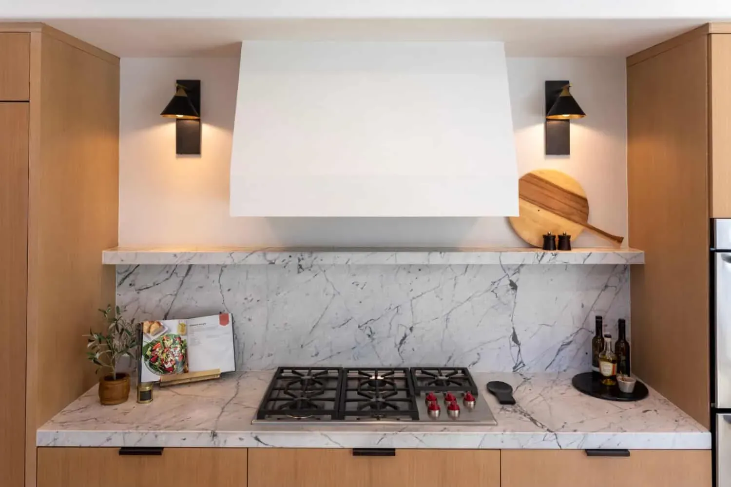 White plaster hood with wall sconces over a marble backsplash and cooktop