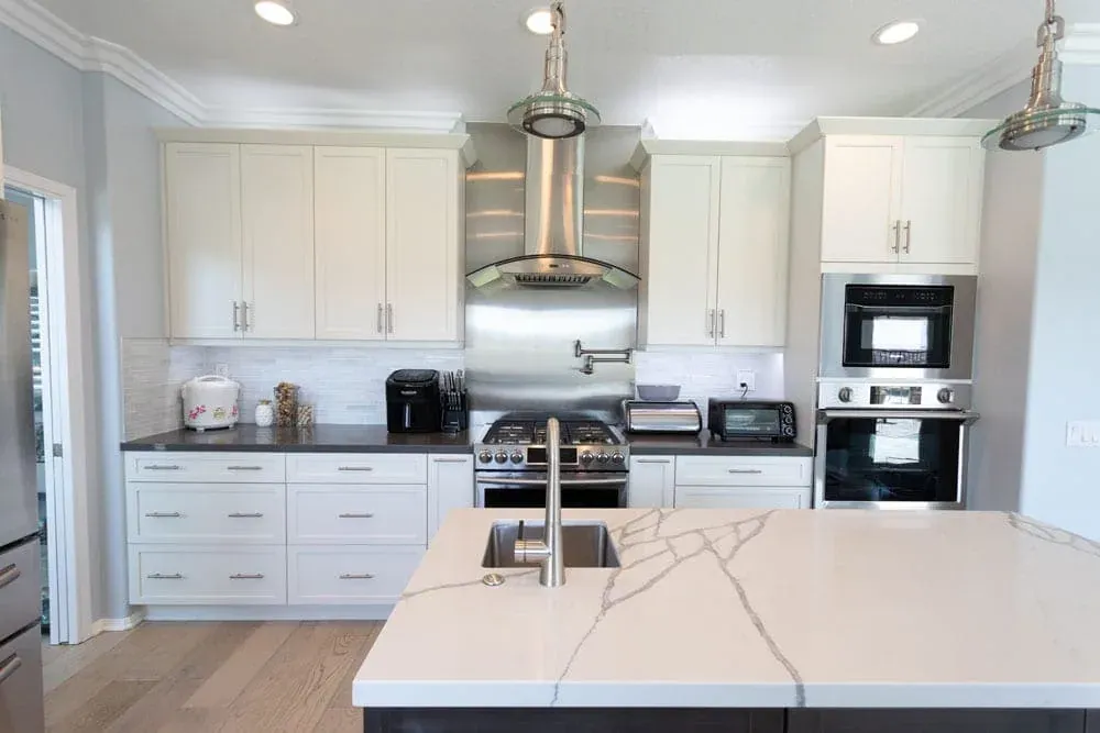 Quartz waterfall island beneath a stainless hood in white cabinetry