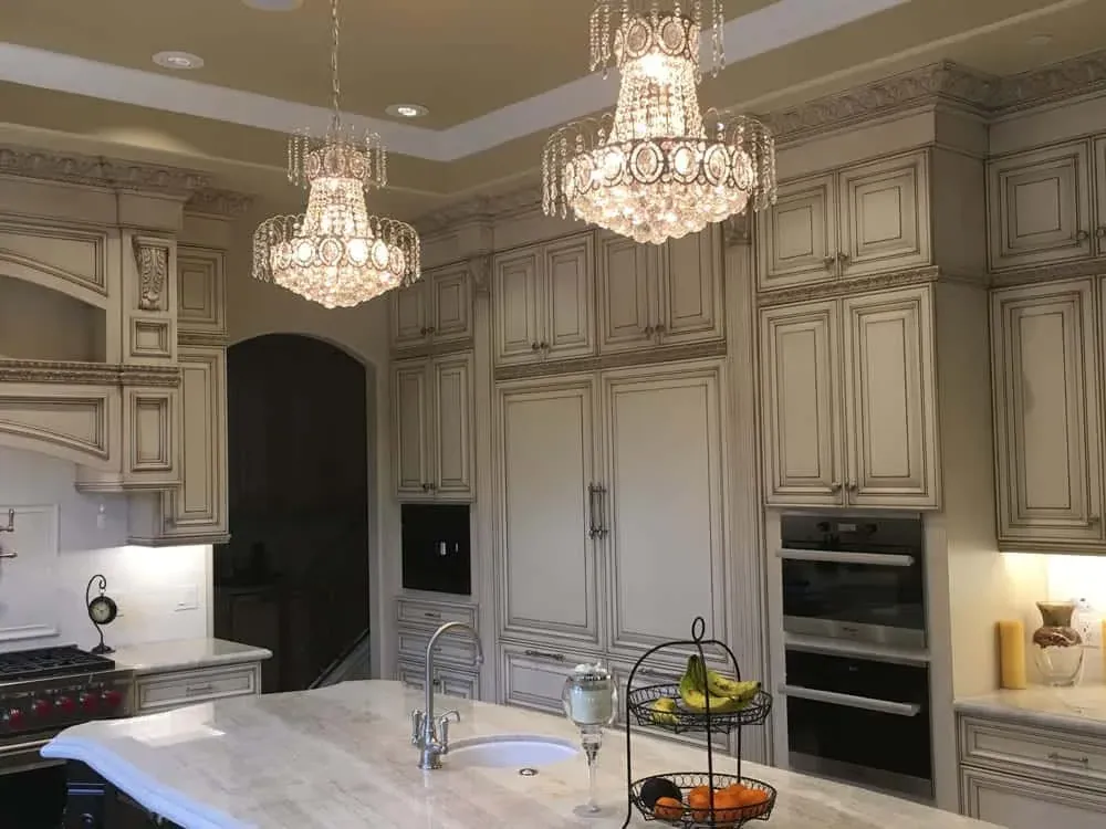 Wide view of an ornate kitchen with paired chandeliers above the island